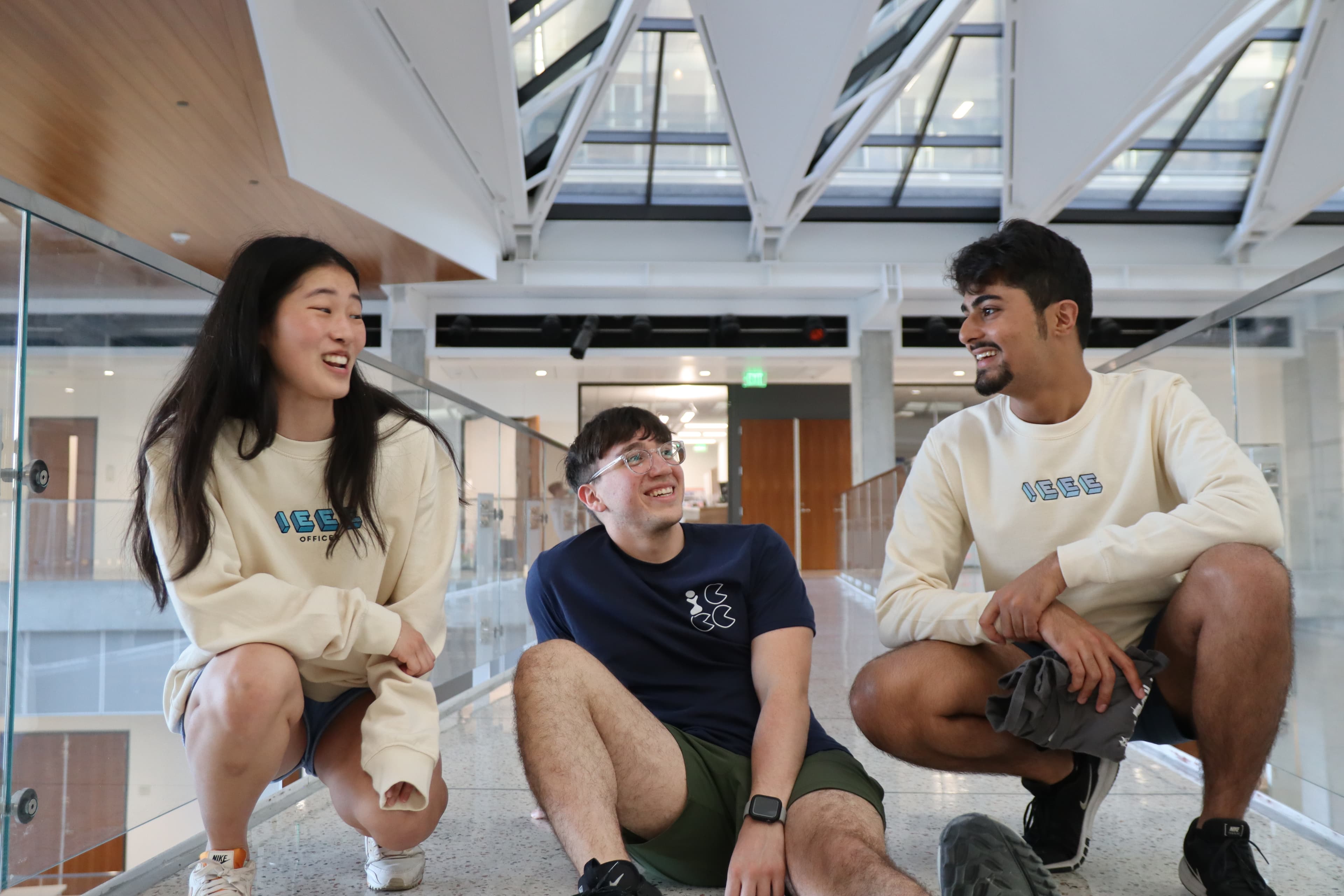 Members in IEEE merch crouch and sit in the middle of path smiling and talking